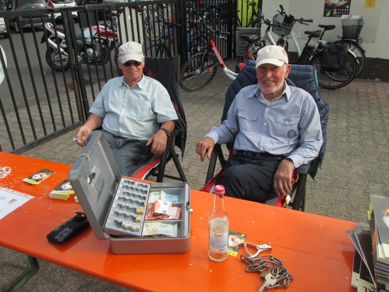 Zwei ältere Männer sitzen an einem Tisch und verkaufen Eintrittskarten für den Mainpokal 2019