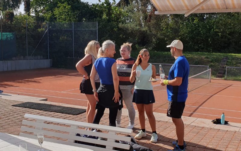 5 Tennis-Mitglieder*innen bei wunderbarem Herbstwetter beim beliebte Mixed-Doppel-Turnier stehen auf der Terasse und unterhalten sich.