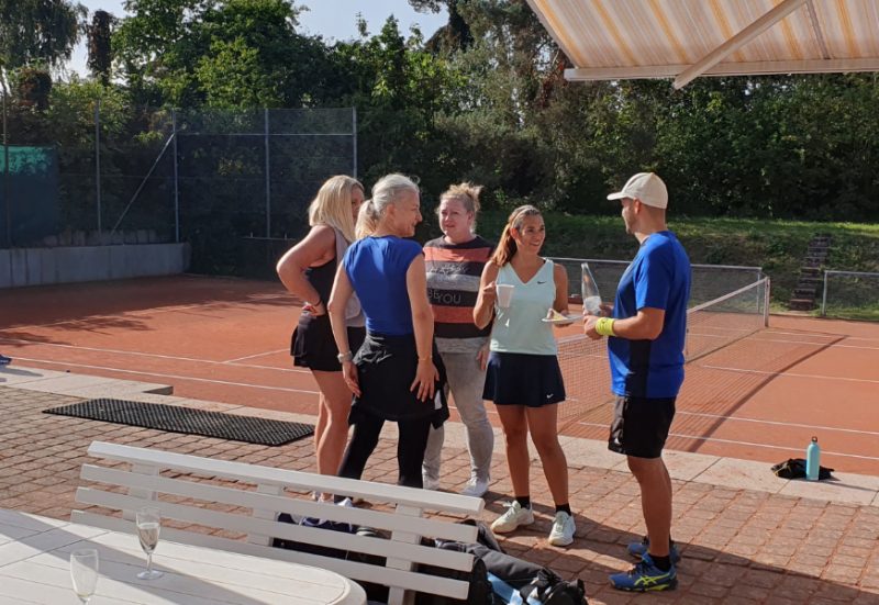 5 Tennis-Mitglieder*innen bei wunderbarem Herbstwetter beim beliebte Mixed-Doppel-Turnier stehen auf der Terasse und unterhalten sich.
