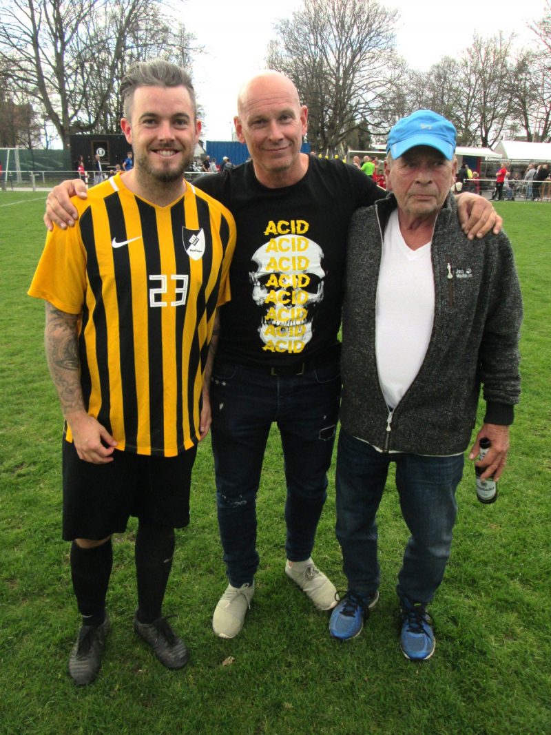 Drei Männer nebeneinander auf dem Fußballplatz: Trainer Marco Schwarzkopf mit Sohn Marvin (Spieler der TSG) und Fan Helmut Thiel.