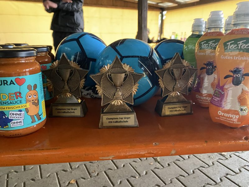 Tisch einer Biergarnitur mit drei Pokalen der FFH Fußballschuhe, 3 blauen Fußbällen, 3 Shan das Schaf Getränken und mehrere Sendung mit der Maus Pasta-Saucen.